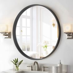 a bathroom sink under a round mirror in front of a white wall with windows and a potted plant next to it