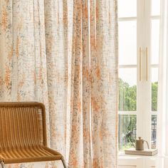 a wicker chair sitting in front of a window with curtains on the windowsill