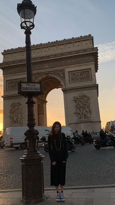 a woman is standing in front of the arc de trioe triumph gate at sunset