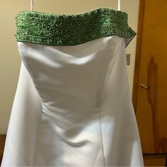 a white and green wedding dress hanging on a door handle with beaded trim around the waist