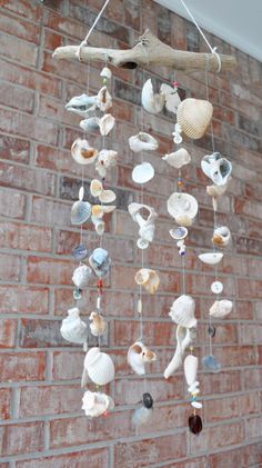 a wind chime hanging from a brick wall next to a tree branch with seashells on it