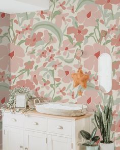 a white dresser sitting next to a wall covered in pink and green floral wallpaper