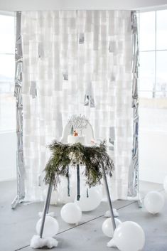 an arrangement of white balloons and greenery in front of a backdrop that looks like snowflakes