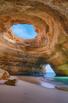 the inside of a cave with blue water and rocks on the beach next to it