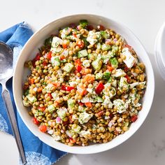 a white bowl filled with corn salad next to a spoon and blue napkin on top of a table