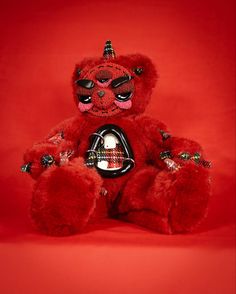 a red teddy bear sitting on top of a red background wearing a party hat and mask