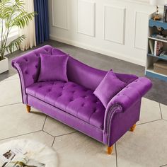 a purple couch sitting on top of a white floor next to a book shelf filled with books