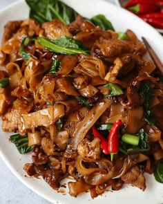 a white plate topped with meat and veggies next to chopsticks on a table