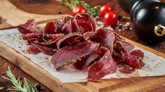 raw meat on a wooden cutting board with tomatoes and peppercorst in the background