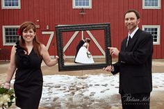 a man and woman standing in front of a red barn holding up a framed photo