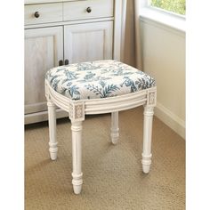 a white bench with a floral upholstered seat and foot rest in front of a window