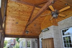 a ceiling fan mounted to the side of a wooden roof over an outdoor living area