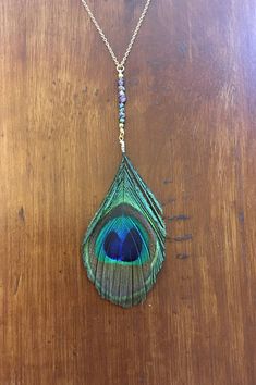 a necklace with a peacock feather hanging from it's side on a wooden table