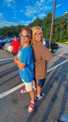 two girls standing in the parking lot with their arms around each other and one girl wearing sunglasses