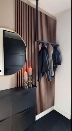 a coat rack with two coats hanging on it next to a wall mounted mirror and candles