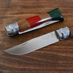 two knives sitting next to each other on top of a wooden table and one has a green handle