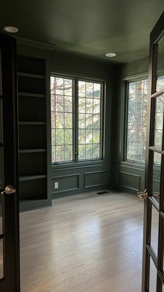 an empty room with wood floors and green walls, two large windows on the far wall