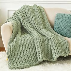 a green knitted blanket sitting on top of a white couch next to a pillow