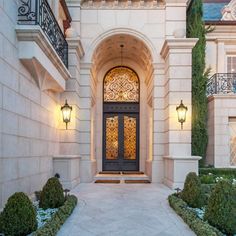 the front entrance to a large home with an arched door and decorative plants on either side