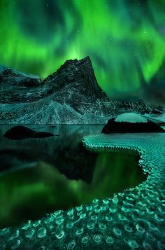 the aurora bore is shining brightly in the sky over water and mountains with ice on them