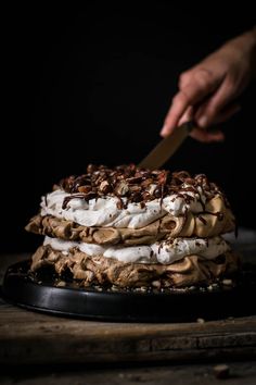 someone is cutting into a layered dessert with whipped cream and pecans on the top