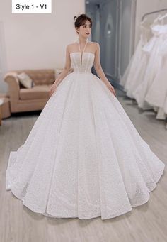 a woman in a white wedding dress standing next to a couch and looking at the camera