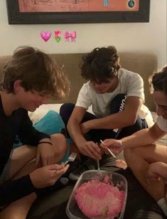 four young people sitting on a bed looking at their cell phones and eating cake together