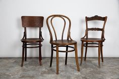 two wooden chairs sitting next to each other in front of a white wall and cement floor