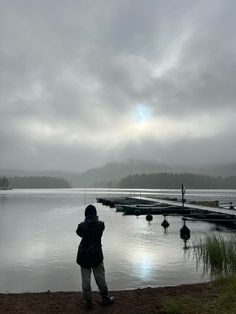 a person standing in front of a body of water with boats on the shore and cloudy skies