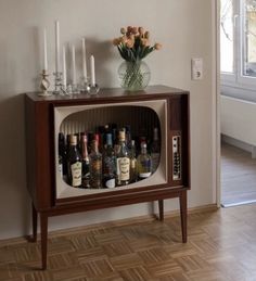 an old fashioned television with liquor bottles and candles on the shelf in front of it