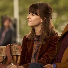 a woman sitting next to a man on top of a wooden bench in front of trees