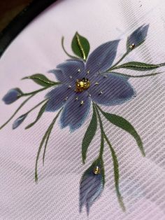 a blue flower on a white cloth with green leaves and water drops in the center