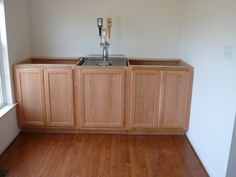 an empty kitchen with wooden floors and cabinets in the corner, next to a window