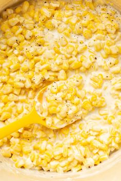 a pot filled with corn and cream on top of a counter next to a wooden spoon