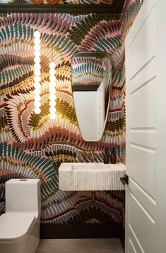 a bathroom with colorful wallpaper and a white toilet next to a mirror on the wall