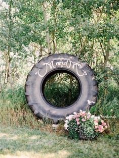 an old tire is sitting in the grass near some flowers and trees with a sign that says mama on it