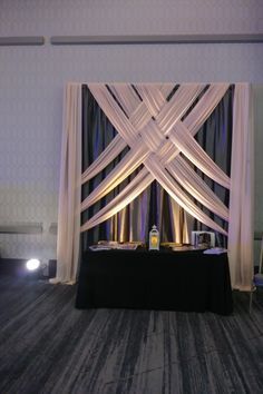 a black table topped with a bottle of wine under a white drape covered wall