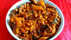 a bowl filled with beans and meat on top of a red tablecloth covered table