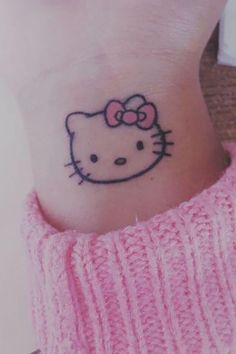 a small hello kitty tattoo on the left side of her right wrist, with a pink sweater underneath it