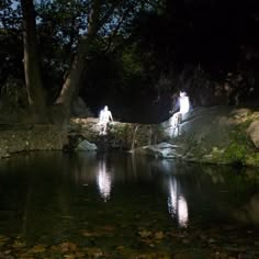 two people standing on rocks in the middle of a pond at night with lights shining