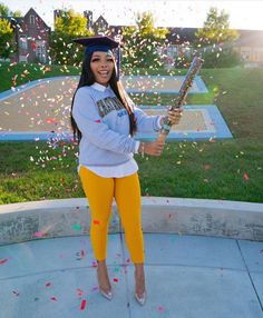 a woman in yellow pants and a gray hoodie holding a baseball bat with confetti all around her