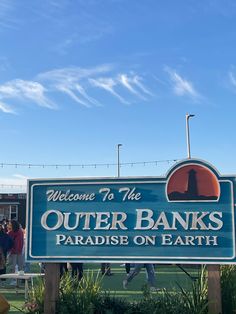 a sign that says welcome to the outer banks paradise on earth with people standing around it