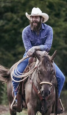 a man riding on the back of a brown horse wearing a cowboy hat and blue shirt