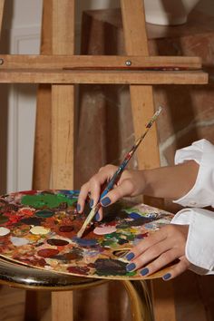 a woman is painting on an easel with paintbrushes