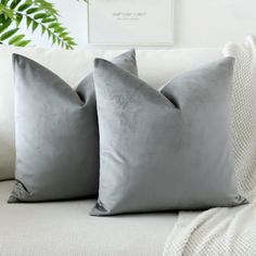 two gray pillows sitting on top of a white couch