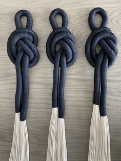 three black and white tasselled wall hangings on a wooden surface with one knot tied in the middle