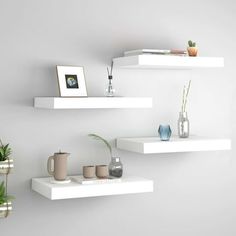 three white floating shelves with plants and vases on them in the corner of a room