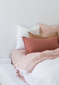 a white bed topped with lots of pink and brown pillows next to a wall mounted clock