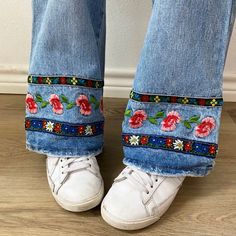 someone wearing white shoes and jeans with flowers on the side, standing in front of a wall