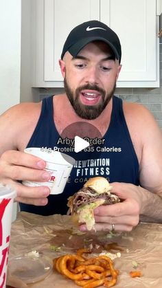 a man in a tank top is eating a sandwich and drinking a drink from a cup